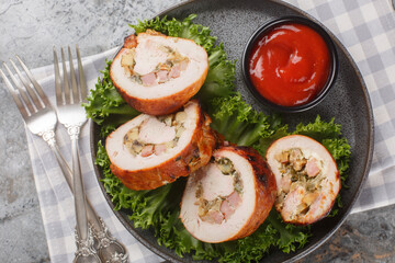 Festive sliced ​​turkey fillet roll with bacon, onions and mushrooms served with ketchup close-up in a plate on the table. Horizontal top view from above