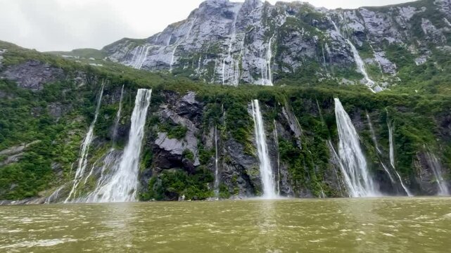 spectacular Four Sisters Waterfalls falling from the dramatic mountain cliff during a heavy rainfall - Ferry Cruise Through Milford Sound fiord, Fiordland National Park, South Island, New Zealand