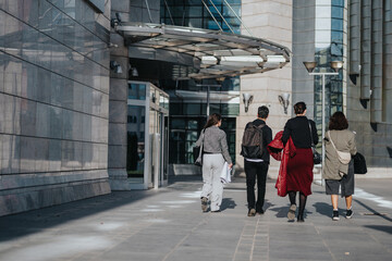 Obraz premium A diverse group of business people walking together past a contemporary office building, symbolizing teamwork, collaboration, and success in a corporate setting.
