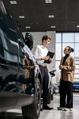 A car dealer in a modern car dealership advises a customer on buying or leasing a new car. The...