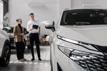 A car dealer in a modern car dealership advises a customer on buying or leasing a new car. The concept of an expensive purchase or lease of a modern car. 