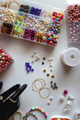 Hand figurine, colorful friendship bracelets, necklaces, various beads and DIY supplies on the table. Making jewelry at home. Flat lay.