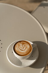 A latte with foam art in a textured ceramic cup, set against a neutral backdrop.