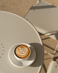 A latte with leaf-shaped art sits on a table bathed in warm sunlight.