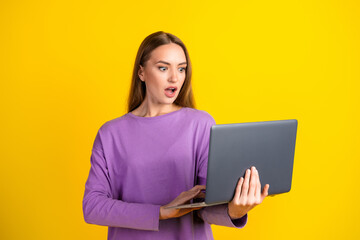 Fototapeta premium Surprised young woman with laptop against colorful yellow background showcasing vibrant emotions and appealing casual style