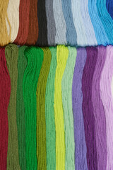 A close-up photograph of a variety of colorful embroidery threads arranged in parallel rows,...