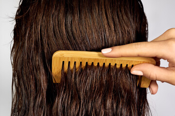 A person is gently combing through wet, dark brown hair using a wide-tooth bamboo comb
