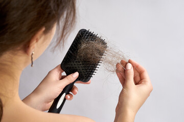 A woman is holding a hairbrush filled with a significant amount of shed hair. She is gently pulling...