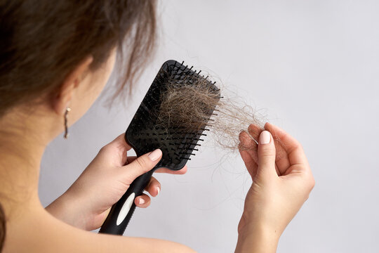 A woman is holding a hairbrush filled with a significant amount of shed hair. She is gently pulling the hair out of the brush, likely examining it.
