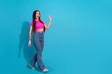 Cheerful young woman in casual attire posing enthusiastically against a vibrant blue background