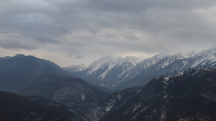 Obraz premium Snow-covered mountain range under grey sky, power lines visible, serene wintry landscape.