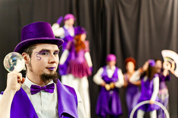 Magician wearing purple costume and top hat holding crystal ball performing with circus troupe in...