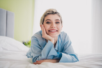 Young cheerful woman relaxing indoors on a cozy bed wearing blue sleepwear, representing comfort