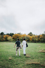 Fototapeta premium Two friends walk in a serene, grassy field under a cloudy sky during autumn. The scene evokes feelings of tranquility, companionship, and nature's beauty. Ideal for concepts of friendship and outdoor