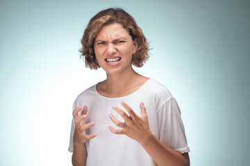A young woman with short curly hair showing frustration and anger, wearing a white shirt against a...