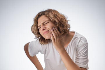 Young woman grimaces in pain while pressing her cheek, showing clear signs of oral discomfort due...