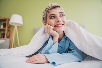 Young woman smiling in a cozy bedroom, relaxing in bed with soft lighting and a serene atmosphere...