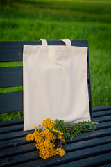 White canvas tote bag mockup template with long handles and wild flowers on the bench outdoor