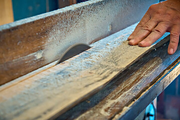 Close-up of a male carpenter's hand feeding a board to a table saw to cut it in the workshop. Selective focus