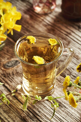 A glass cup of coltsfoot tea with fresh coltsfoot flowers