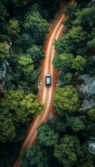 Car drives down winding dirt road through forest, aerial perspective