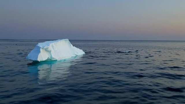 A serene video captures a lone iceberg floating in calm waters at sunset. The wide-angle shot emphasizes the vastness of the ocean and sky. Live desktop wallpaper.