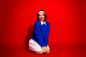 Fototapeta premium Young woman in vibrant blue sweatshirt posing cheerfully against a bold red background, embracing confidence and style