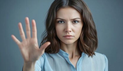 Fototapeta premium Woman Showing Stop Gesture with Hand, Serious Expression, Blue Shirt, Gray Background