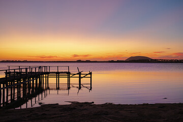 Obraz premium Sunset over the lake with the dormant volcano, Mount Elephant, in the background and wood jetty in the foreground, Lake Tooliorook, Victoria, Australia