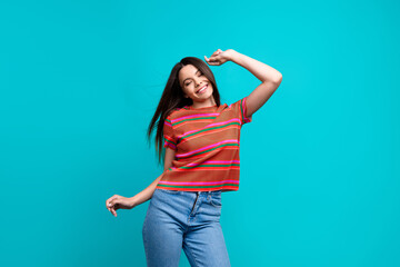 Cheerful young woman striking a playful pose in casual striped top and denim on a vibrant turquoise background