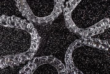 Invisible dental teeth brackets tooth aligners on black background. Plastic braces dentistry retainers to straighten teeth.