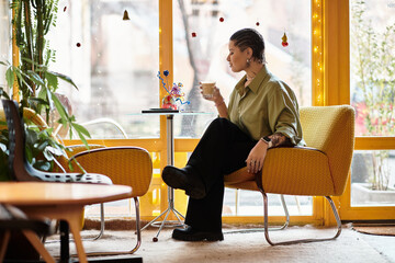 Charming young woman enjoys a cozy moment at a vibrant cafe during a rainy afternoon