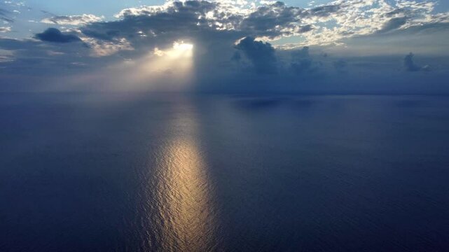 Aerial video moving towards the sun's rays breaking through the clouds over Cozumel's vast ocean. Witness the golden light reflecting on the tranquil waters