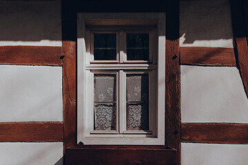 Old wooden house with a charming window dressed in lace curtains, showcasing rustic architecture in a tranquil setting
