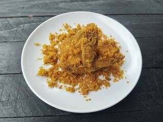 Ayam goreng serundeng or Fried chicken with fried grated coconut on plate with black wooden table background