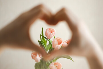 Hands of man making heart over pink tulips at home, close up.
