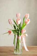 A bouquet of delicate pink tulips in a glass vase on a wooden table.