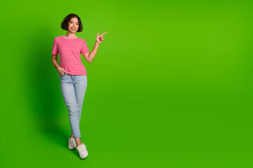 Smiling young woman in casual attire posing on green background with a cheerful gesture, exuding style and confidence