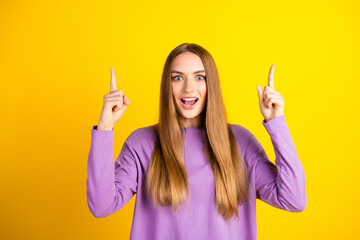 Cheerful young woman with long brown hair gestures enthusiastically on a vibrant yellow background...