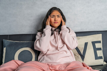 Young woman suffering from strong headache while relaxing on sofa at home