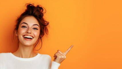 Beautiful girl posing on orange background and pointing finger at place for advertisement and text