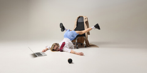 Office worker balancing upside down on chair, while working on laptop, reflecting instability of...