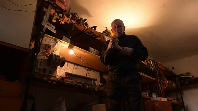 In the warm glow of a workshop lamp. Grandpa sharpens an axe in his workshop. Surrounded by the organized chaos of machinery and equipment.
