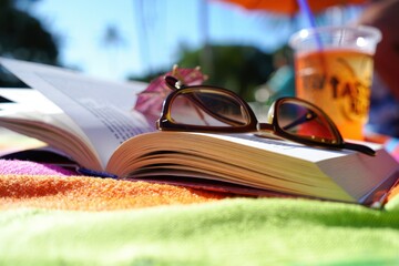 Relaxing summer scene with open book and sunglasses on vibrant towel at beach