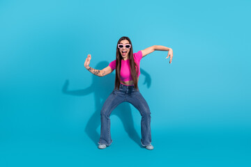 Energetic woman in casual outfit posing playfully with quirky hand gestures against a vibrant blue...