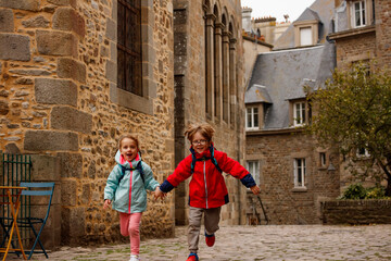 Kids with backpacks joyfully run on a historic cobblestone path