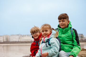 Naklejka premium Three kids smile at beach with Saint-Malo town behind, France