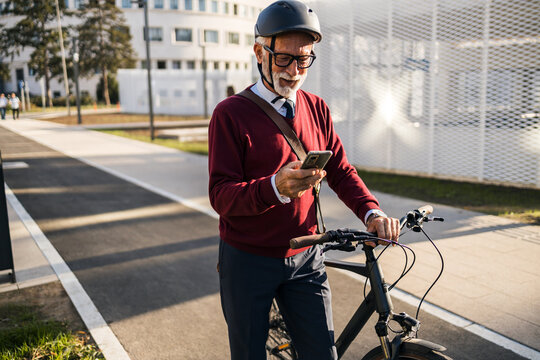 Senior Businessman Smiling While Using Smartphone During Cycling Commute in City
