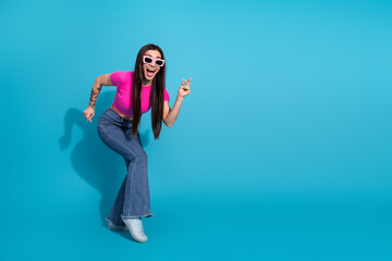Young stylish woman in pink top and sunglasses posing dynamically on a bright blue background...