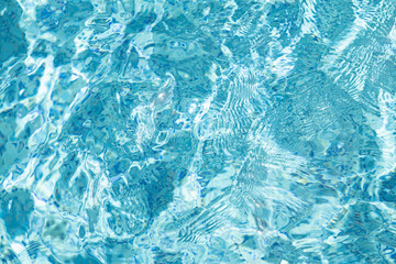 Transparent blue water in swimming pool with waves in sunlight. Abstract surface texture or nature background. Water surface